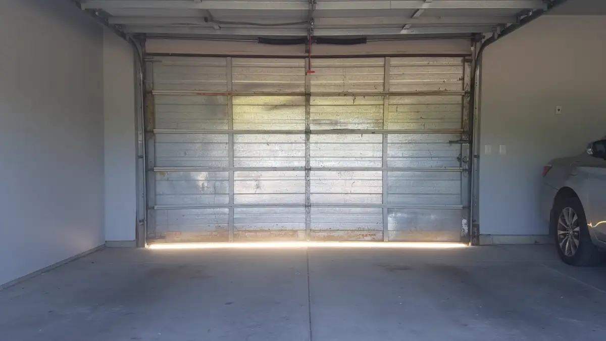 The closed metal garage door has a torsion spring and a car parked inside.